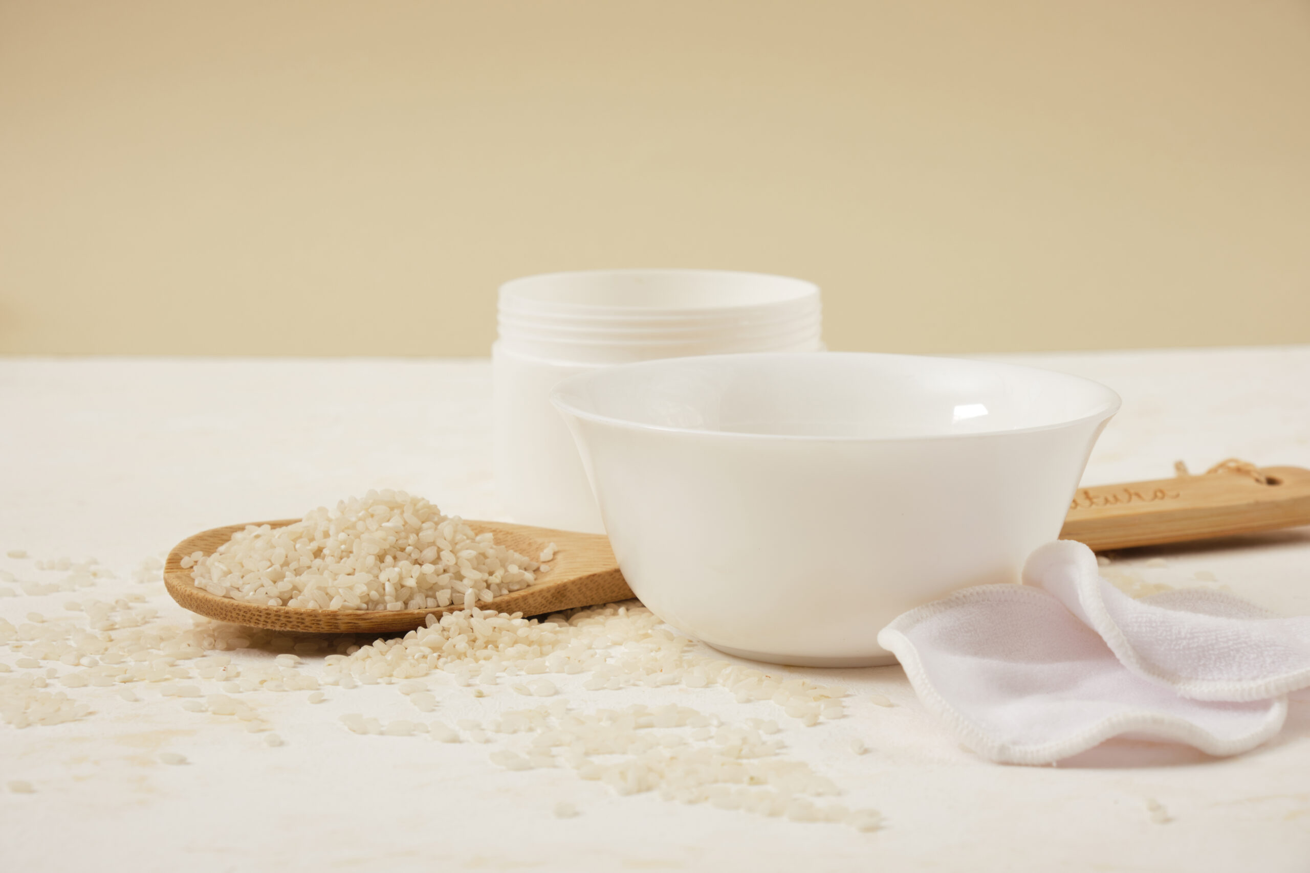 white bowls with rice and rice water, fermented skin and hair care products, organic cosmetics, light background, rice water mask, rice grains spoon