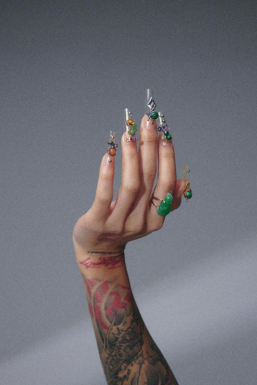 A hand wearing Coca Michelle Frequency Collection nail charms